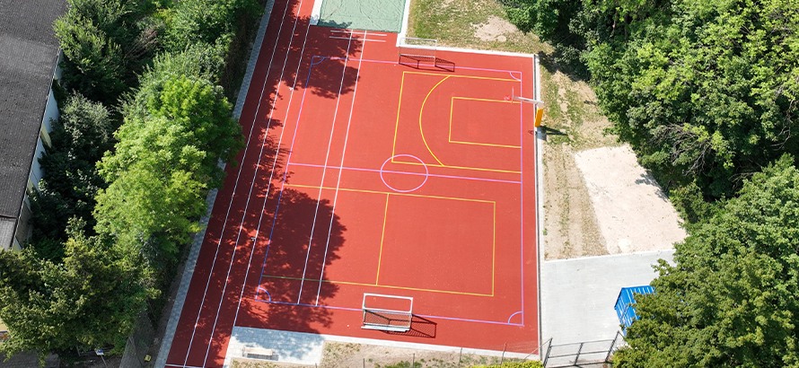 Luftaufnahme eines sanierten roten Allwetterplatzes in Erding mit Spielfeldmarkierungen für mehrere Sportarten